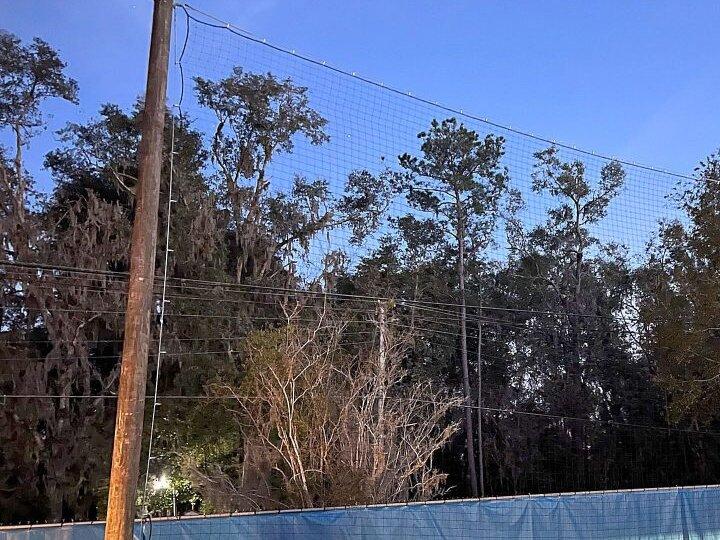 Soccer field perimeter netting on wood poles above a blue windscreen at Epiphany Catholic Church