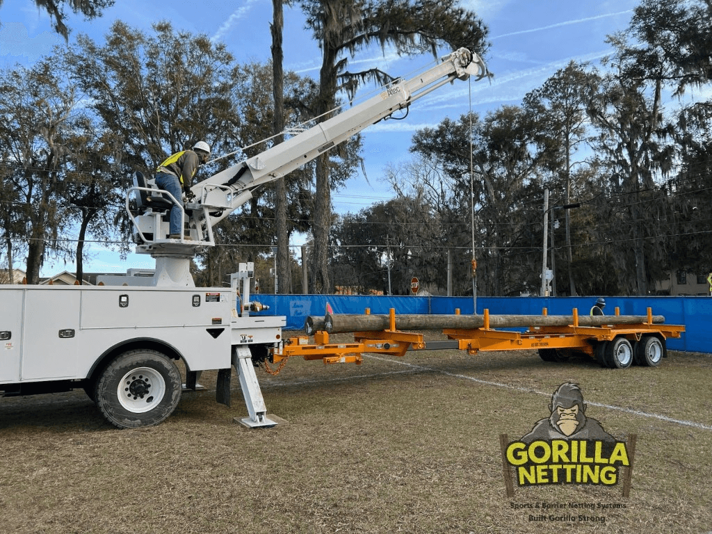 Utility truck and crane setting wooden netting poles on a soccer field