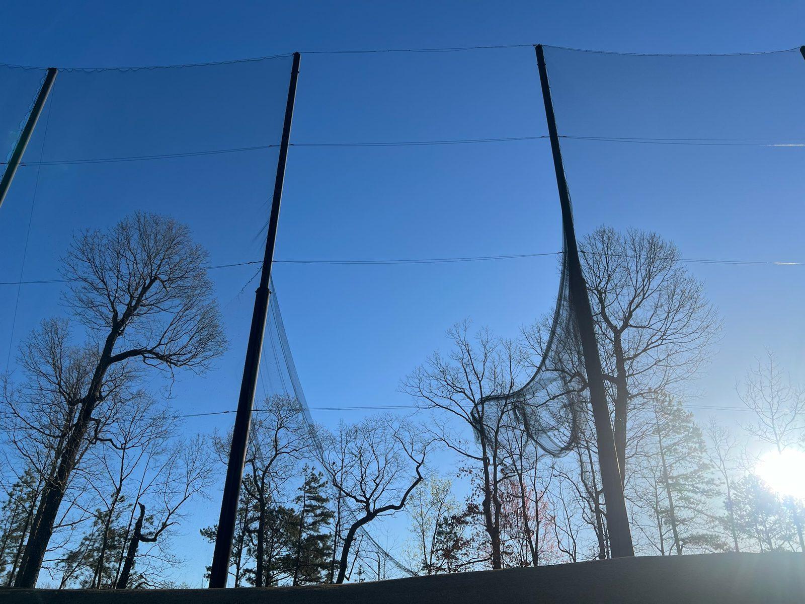 Old range netting sagging off its cable between two poles, Full-height driving range netting enclosure at Dunwoody Country Club in Atlanta