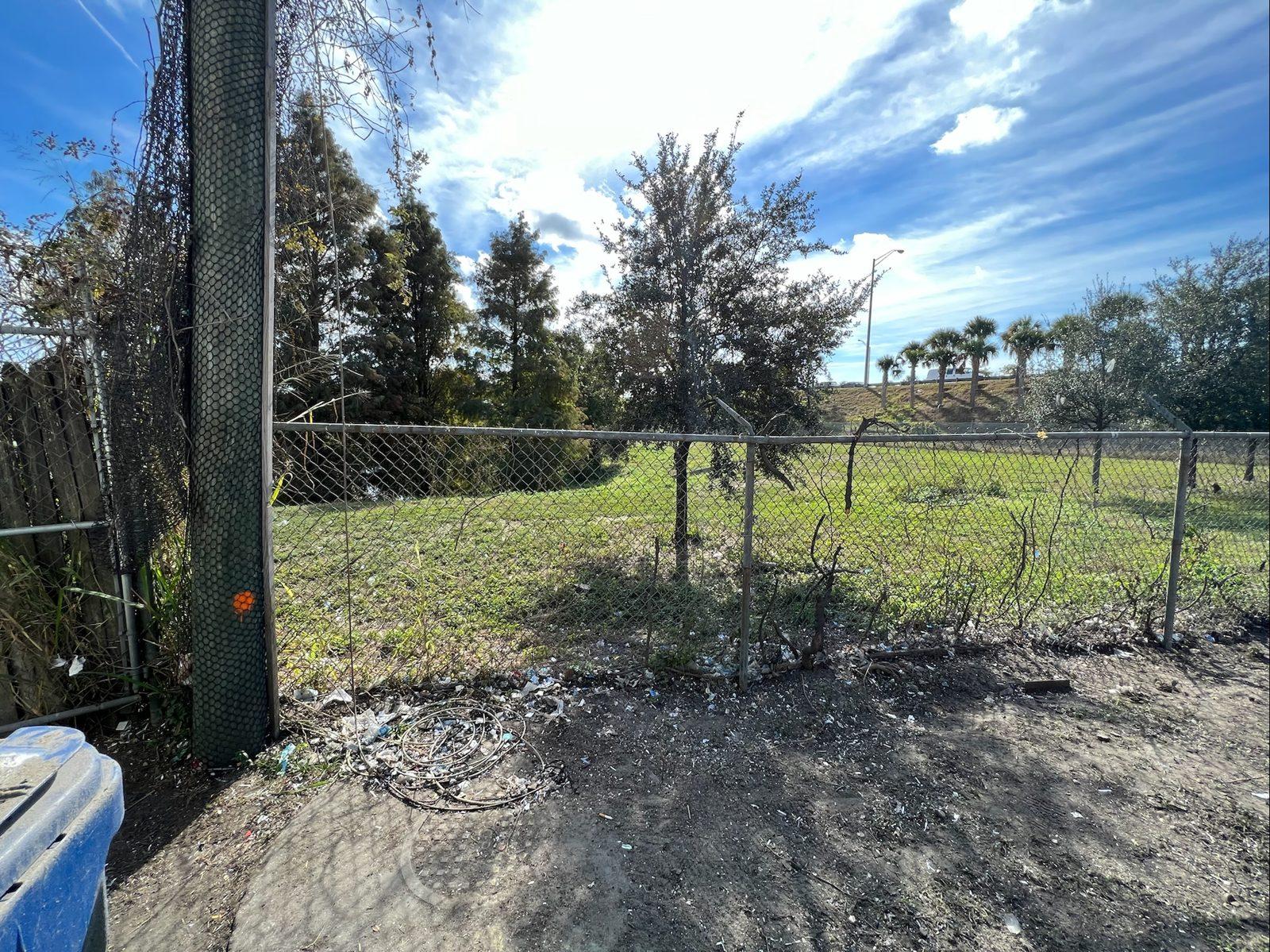 Before: The south fence line before the new system: an old pole wrapped in worn netting beside the chain link fence. Barrier Netting Installation for Waste Connections