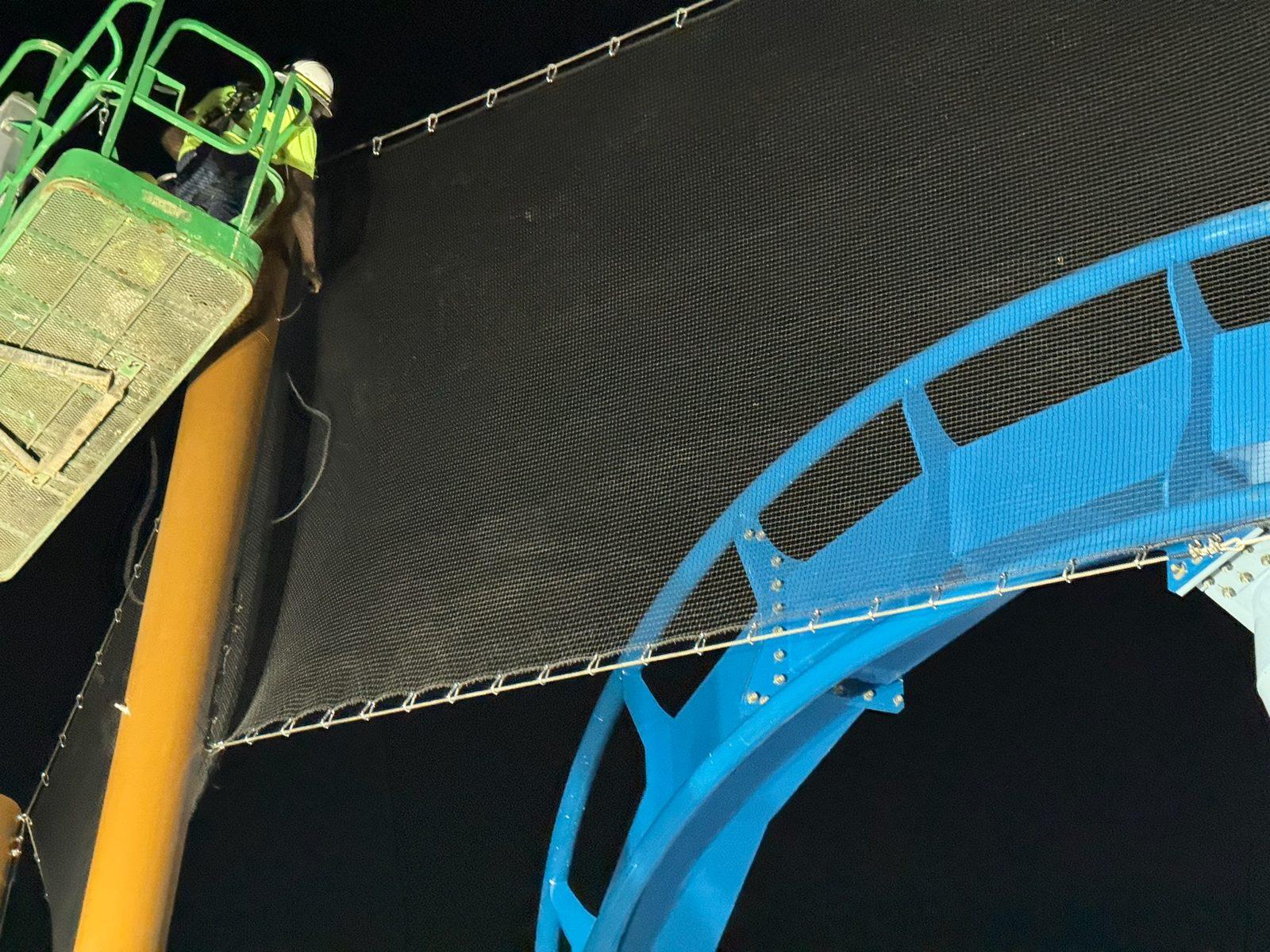 During: Crew in a lift attaching a black mesh panel to a steel pole beside the coaster track. Overhead Netting at Busch Gardens Tampa Bay