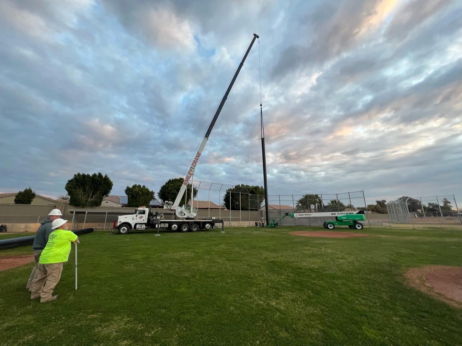 During: Crane raises the first steel pole into place at dawn. Baseball Backstop Netting at Millennium High School