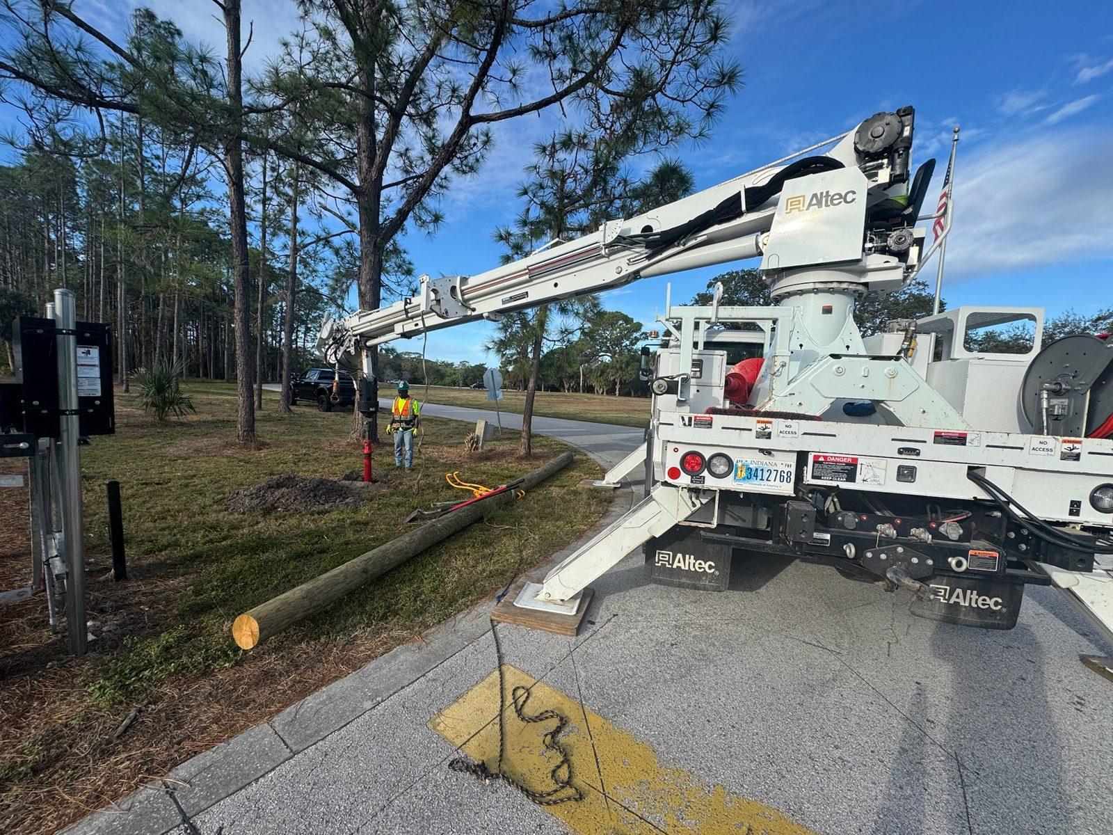 During: Boom truck lowering a wood pole into place beside a park gate. Park Entrance Pole Setting Across Pinellas County