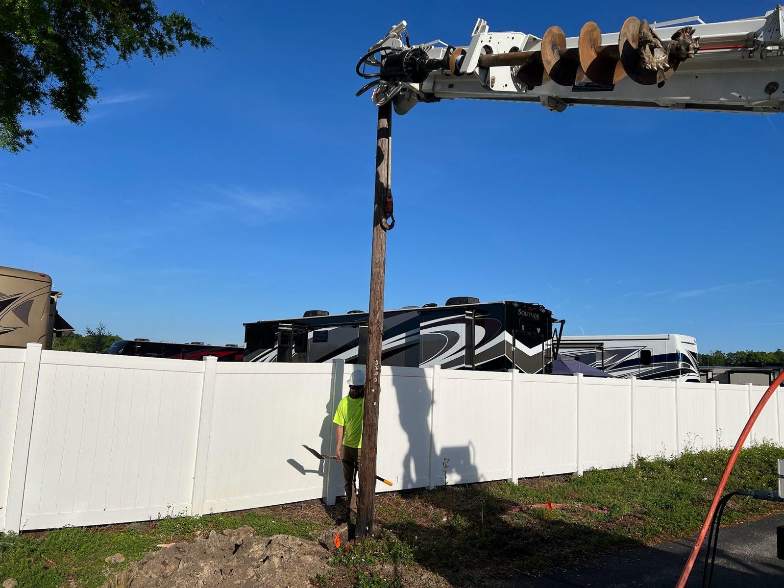 During: Boom truck lowers a wood pole into place along a vinyl fence. Wood Pole Setting at an RV Park in Central Florida