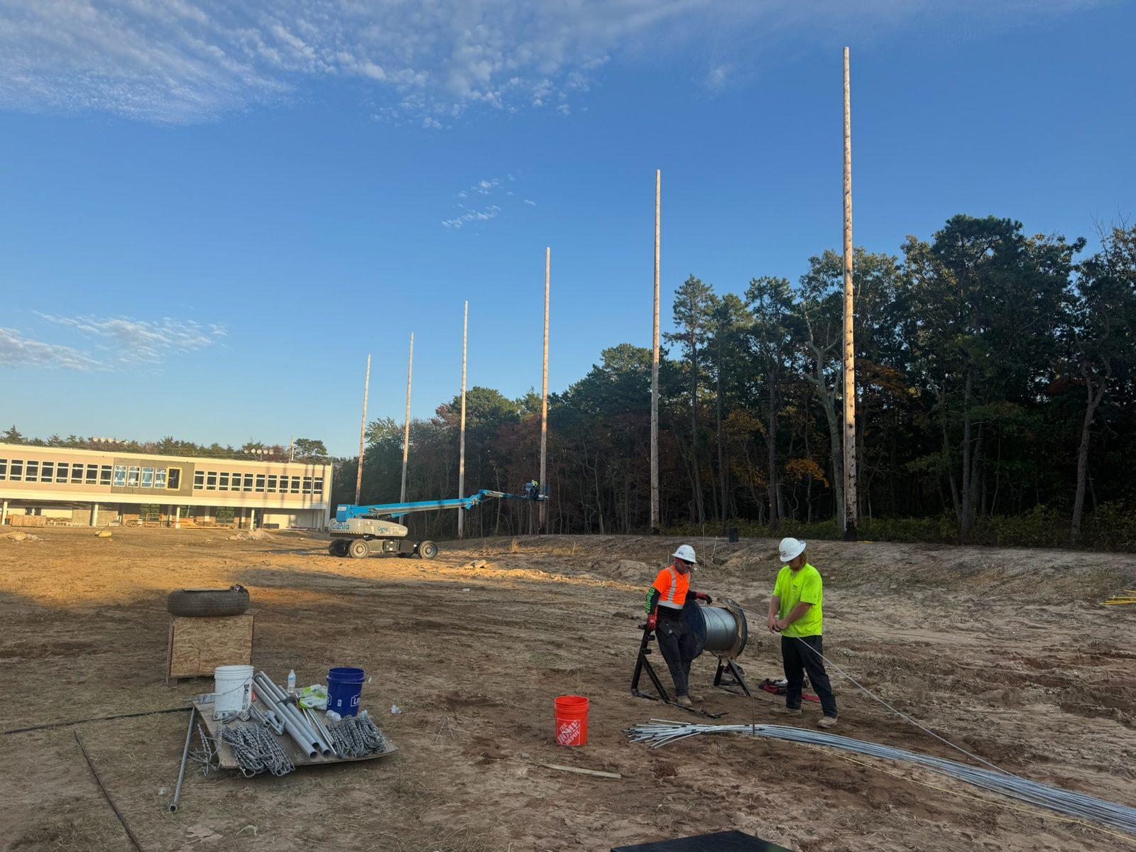 During: Crew paying out cable from a reel below the new poles. Driving Range Netting at Toms River Golf Center