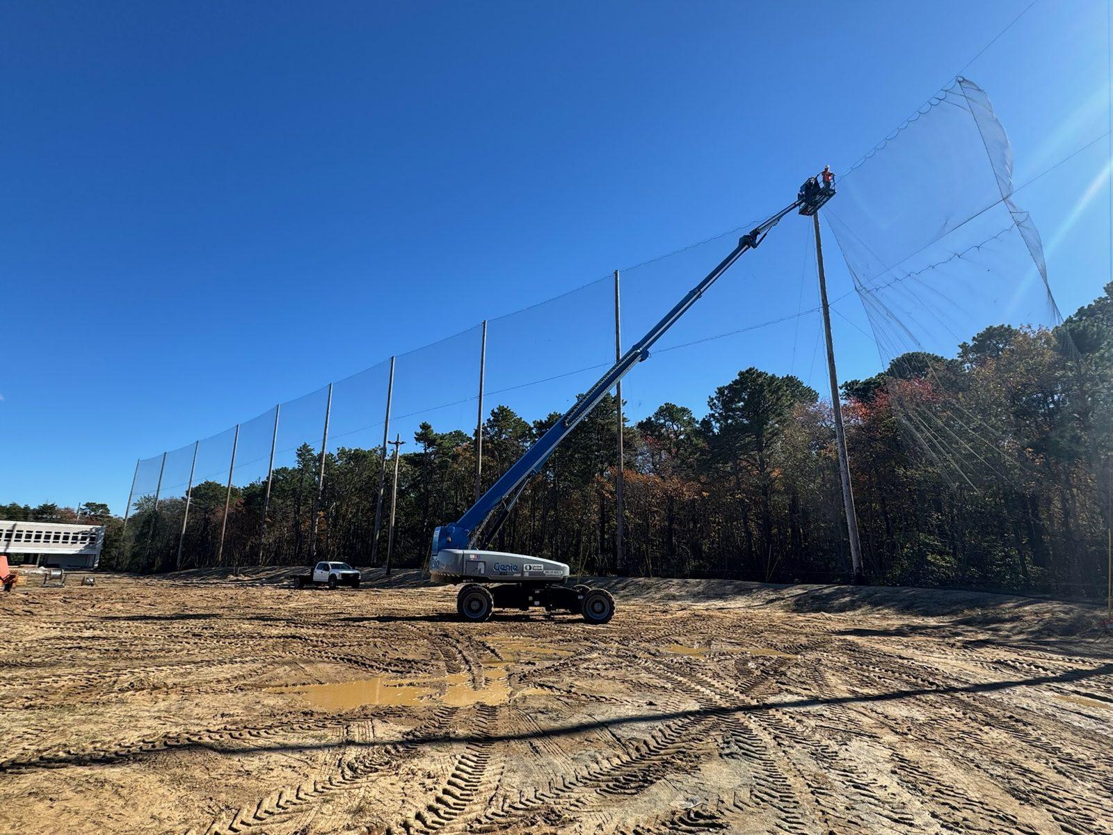 During: Crew in a boom lift hanging netting on the tree line side. Driving Range Netting at Toms River Golf Center