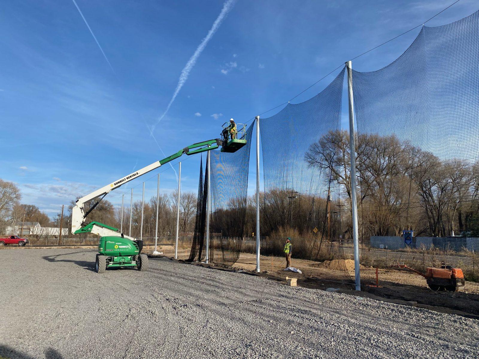 During: First panels of black netting hung from the top cable, lift crew working the next bay. Perimeter Netting at West Las Vegas Middle School