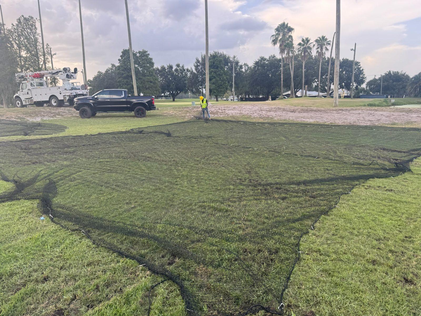 During: New black netting laid out on the grass before hanging. Perimeter Netting Replacement at the YMCA Par 3 Course in Lakeland