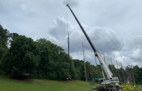 A crane lifts a wooden support beam into place for driving range netting.
